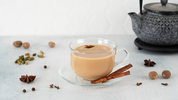 Masala thé chai dans une tasse en verre avec théière traditionnelle. Délicieuse boisson indienne - thé noir épicé avec des ingrédients : cannelle, gingembre, muscade, cardamome, anis, miel, clous de girofle et lait. Vue latérale — Photo
