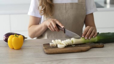 Kadınların elleri tahta kesme tahtasında organik taze pırasa kesiyor. Taze yeşil pırasa dilimleri. Evde yemek pişirmek..