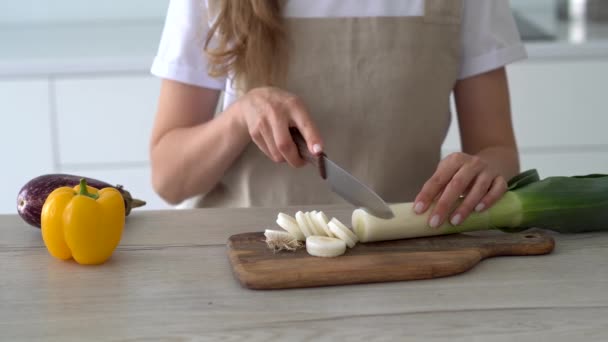 Dámské ruce řežou čerstvý pórek na dřevěné řezací desce. Vaření doma. — Stock video