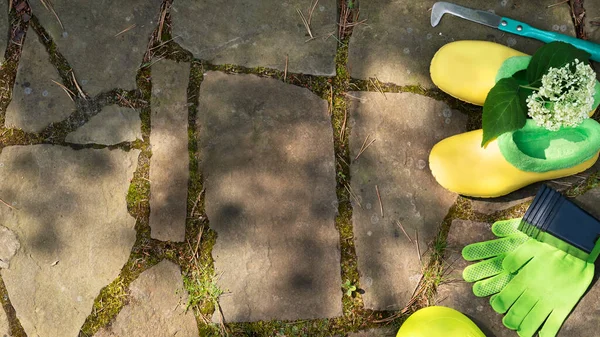 Equipo de jardinería. Pala o pala de jardín, guantes de mano verdes y zapatos de goma con hortensias en el camino de piedra en el jardín. Fondo de granja. Vista superior. Copiar espacio. Enfoque selectivo. — Foto de Stock