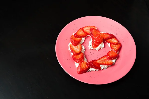 Çilek siyah arka plan üzerine pembe bir tabak içinde kalp şeklinde