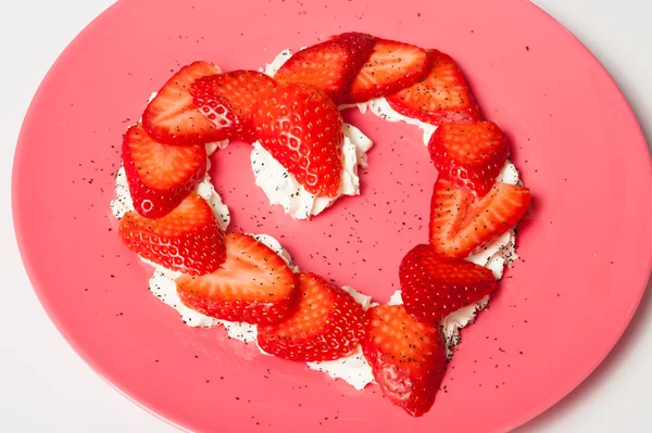 Çilek beyaz arka plan üzerinde pembe bir tabak içinde kalp şeklinde