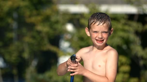Мальчик распыляет воду из шланга — стоковое видео