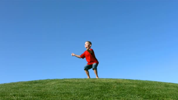 Jongen springen op een heuveltop — Stockvideo