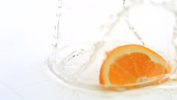 Orangenscheibe spritzt ins Wasser — Stockvideo