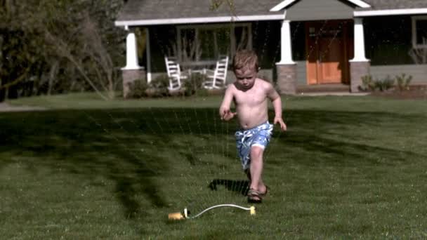 Мальчик бежит через разбрызгиватель — стоковое видео