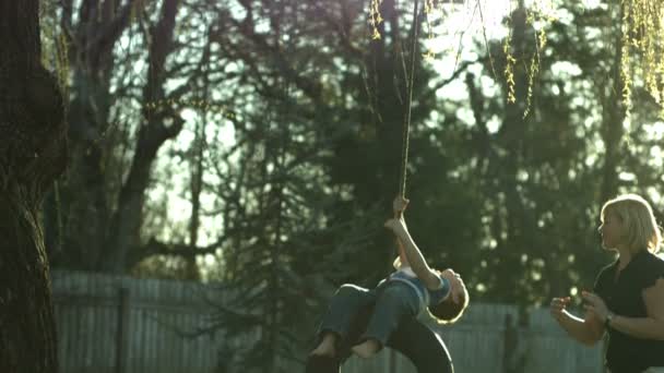 Mom pushing son on tire swing — Stock Video