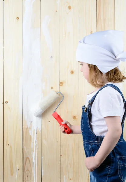 Little girl paints a wooden wall