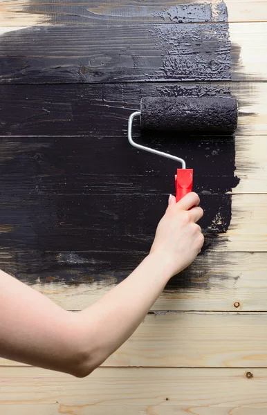 Woman painter paints the wooden wall in black — Stock Photo, Image