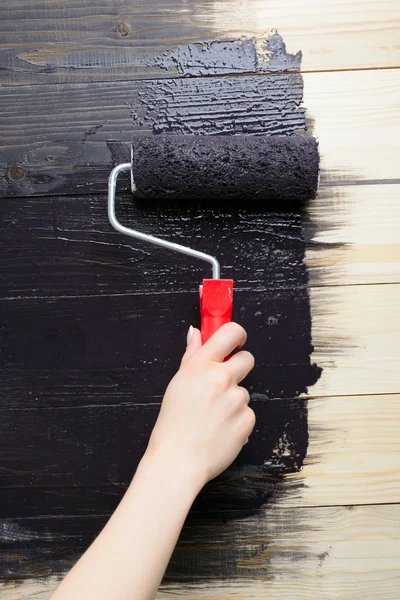 Woman painter paints the wooden wall in black — Stock Photo, Image