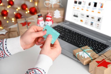 İnternetten Noel alışverişi. Tanınmayan Adam Eller, elinde kredi kartı ile dizüstü bilgisayar kullanarak hediyeler alıyor..