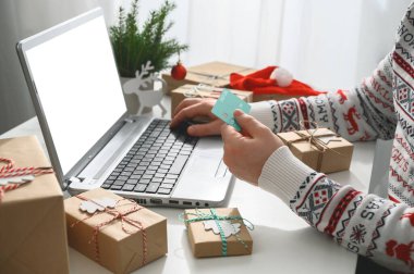 İnternetten Noel alışverişi. Tanınmayan Adam Eller, elinde kredi kartı ile dizüstü bilgisayar kullanarak hediyeler alıyor..