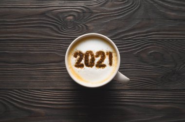 2021 numara, koyu ahşap masada kahve fincanında kapuçino köpüklü yüzeyi. Yemek yaratıcı konsept.