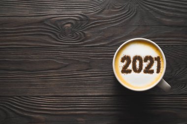 2021 numara, koyu ahşap masada kahve fincanında kapuçino köpüklü yüzeyi. Yemek yaratıcı konsept.