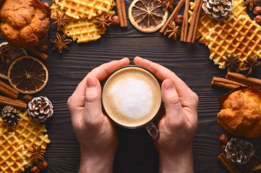 Erkek eller kahve fincanı tutuyor, kurabiyeler ve baharatlar ahşap kırsal alanda. Şık, rahat bir kış yatağı