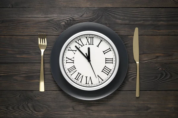 Ünnepi asztal beállítás fekete tál, óra, kés és villa sötét fa asztalon. Szilveszteri táblázat beállítása — Stock Fotó