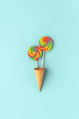 Pastel arkaplanda waffle külahında iki yuvarlak gökkuşağı lolipopu.