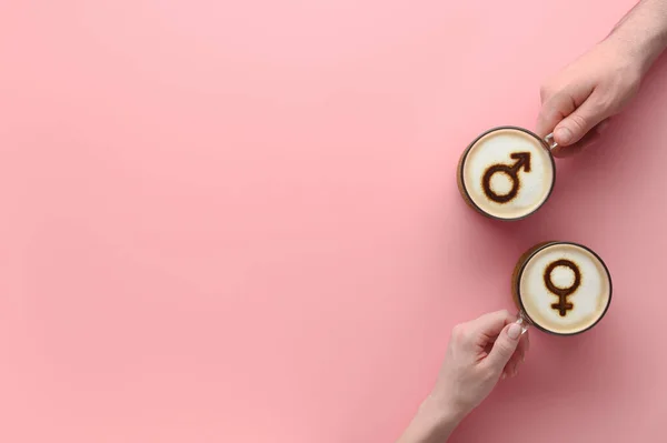 Dłonie zakochanej pary trzymające filiżanki kawy z symbolami Wenus i marsa na piance mlecznej na pastelowym różowym tle — Zdjęcie stockowe