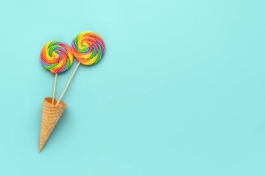 Pastel Cyan arka planda waffle külahında iki yuvarlak gökkuşağı lolipopu. Minimum bileşim, düz konum, üst görünüm, kopyalama alanı. Tatil tebrik kartı. LGBT kavramı