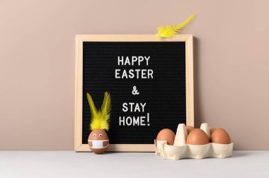 Paskalya tatili konsepti 2021. Yumurtadan yapılan Paskalya tavşanı koruyucu yüz maskesi takıyor ve siyah keçeli mektup panosunda 