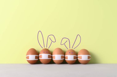 Yeni normal Paskalya tatili konsepti. Paskalya yumurtaları ve pastel yeşil arka planda koruyucu maskeler takan sevimli tavşanlar. Şenlik dekorasyonu. Boşluğu kopyala