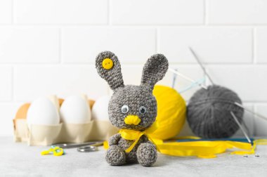 Paskalya işçiliği. El yapımı oyuncak Paskalya tavşanı ve sepetteki örgü aksesuarları. Beyaz tuğla zemin. Seçici odak