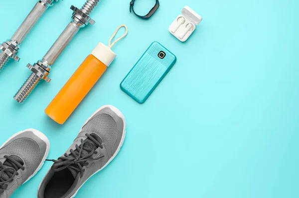 Sports background. Equipment for training and outfit on teal background: dumbbell, fitness tracker, sneakers, smartphone. Fitness, workout at home. Knolling flat lay composition, top view, copy space