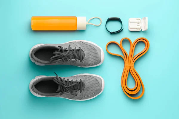 Sports background. Equipment for training and outfit on teal background: expander, fitness tracker, sneakers, bottle juice. Fitness, workout at home. Knolling flat lay composition, overhead view