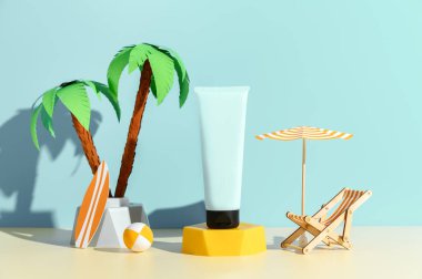 Güneş kremi reklam şablonu, podyumda güneş kremi modeli, minyatür plaj sandalyesi, palmiye ağacı ve şemsiyeyle süslenmiş. Mavi arkaplan