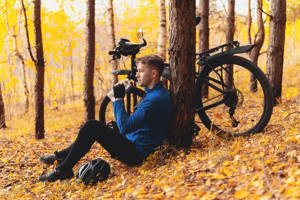 Rozluźnienie stresu, proste przyjemności i trening na świeżym powietrzu. Zmęczony rowerzysta siedzi na jesiennych liściach w lesie i odpoczywa. Charakter z naturą Zdjęcie Stockowe