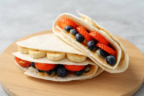 Tortilla de cocina con diferentes rellenos de mantequilla de maní, plátano, fresa, arándanos, almendras. Tendencia alimentaria — Foto de Stock