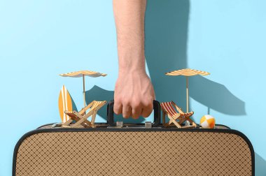 Concept of summer travelling or beach rest. Close up of human hand holds suitcase on a blue background clipart