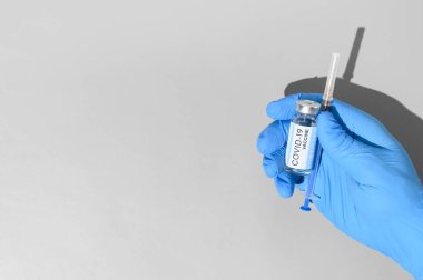 Coronavirus vaccination concept. Hand in medical glove holds syringe and ampoule with the vaccine against COVID-19 on gray background. Top view, copy space