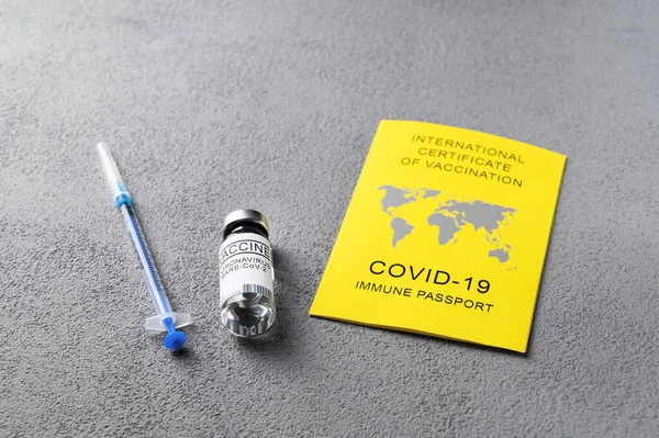 Traveling Immune passport, as proof vaccinated against Covid-19. Yellow International Certificate of Vaccination, syringe, vial with vaccine on gray table