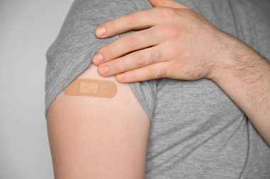 Gri tişört giyen genç bir adam aşıdan sonra kolunu gösteriyor. Salgın covid-19 sırasındaki bağışıklık teması. Yakın çekim, seçici odaklanma