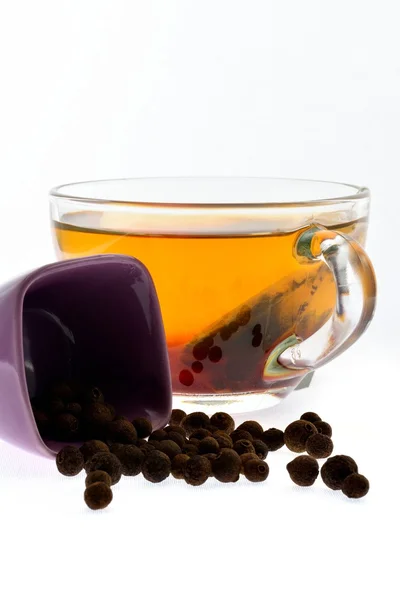 Grains of black pepper and a cup tea — Stock Photo, Image