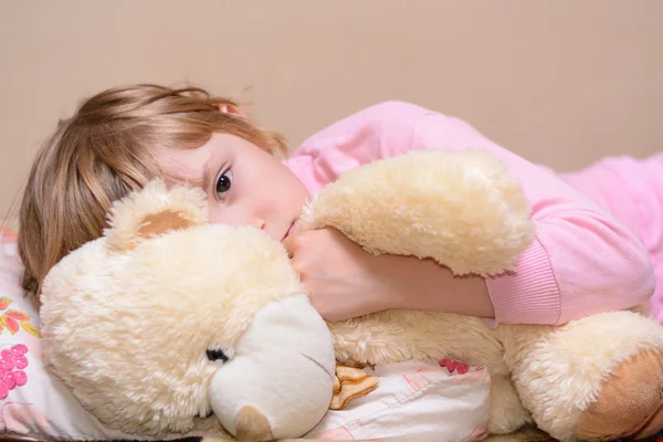 Chica acostada en la cama con un oso de peluche — Foto de Stock