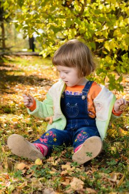 Oturma ve düşen yapraklar ile oynarken küçük bebek