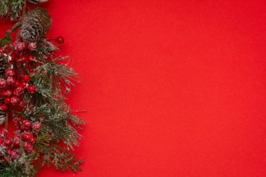 Kırmızı arka planda köknar dalları ve konileri olan kış yılbaşı dekorasyonları.
