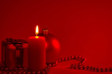 Yanan mum ve Noel süslemesi. Kırmızı arka plan. Şenlikli, sade bir sahne.