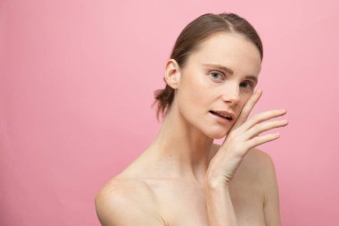 Güzel, şehvetli, üstsüz esmer kadın pembe arka planda yalnız duruyor, poz veriyor. Mutlu kadın model. İnsani duygular ve duygular. Çıplak makyaj. Spa