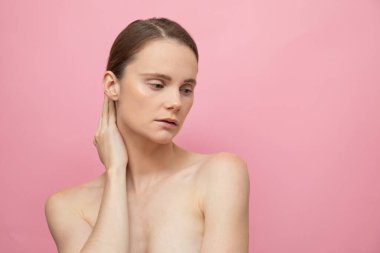 Güzel, şehvetli, üstsüz esmer kadın pembe arka planda yalnız duruyor, poz veriyor. Mutlu kadın model. İnsani duygular ve duygular. Çıplak makyaj. Spa