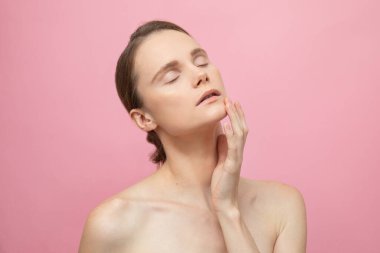 Güzel, şehvetli, üstsüz esmer kadın pembe arka planda yalnız duruyor, poz veriyor. Mutlu kadın model. İnsani duygular ve duygular. Çıplak makyaj. Spa