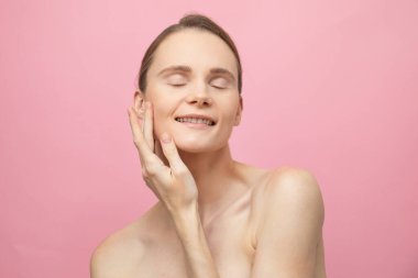 Güzel, şehvetli, üstsüz esmer kadın pembe arka planda yalnız duruyor, poz veriyor. Mutlu kadın model. İnsani duygular ve duygular. Çıplak makyaj. Spa