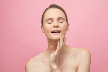 Güzel, şehvetli, üstsüz esmer kadın pembe arka planda yalnız duruyor, poz veriyor. Mutlu kadın model. İnsani duygular ve duygular. Çıplak makyaj. Spa