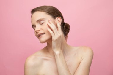 Güzel, şehvetli, üstsüz esmer kadın pembe arka planda yalnız duruyor, poz veriyor. Mutlu kadın model. İnsani duygular ve duygular. Çıplak makyaj. Spa