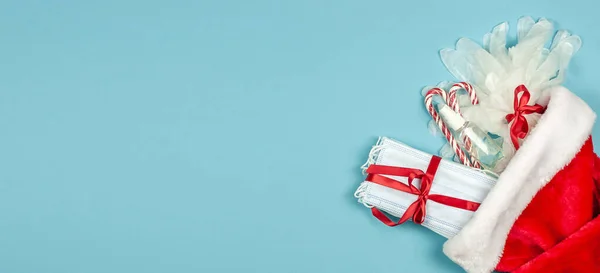 Maske, eldiven, antiseptik ve mavi arka planda Noel Baba şapkası takan bir steteskop. En iyi hediye 2021 Banner.