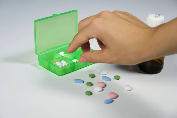 ills,green pill box and young woman hand in white background. Hand taking medicine from green box.