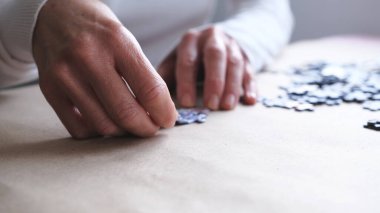 Yapboz parçaları tutan bir kadın. Beyaz kazaklı kadın evde yapboz çözmeye çalışıyor..