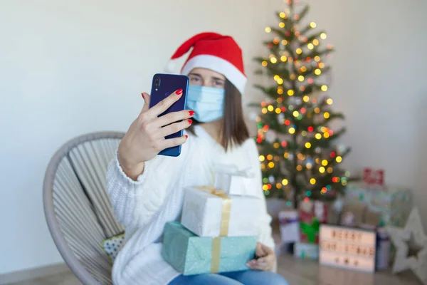 Tıbbi Maskeli Bir Kadın Noel Ağacının Yanında Hediye Kutularıyla Telefonda — Stok fotoğraf